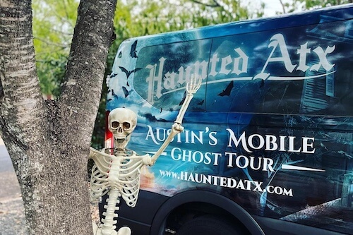 Haunted ATX team wearing HATX shirts while sitting on the hood of the black hearse next to the van